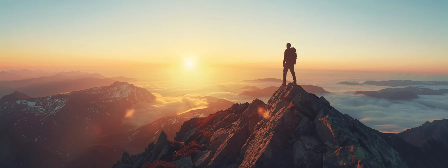 a lone hiker stands atop a majestic mountain peak, gazing out at a breathtaking sunrise over the horizon.