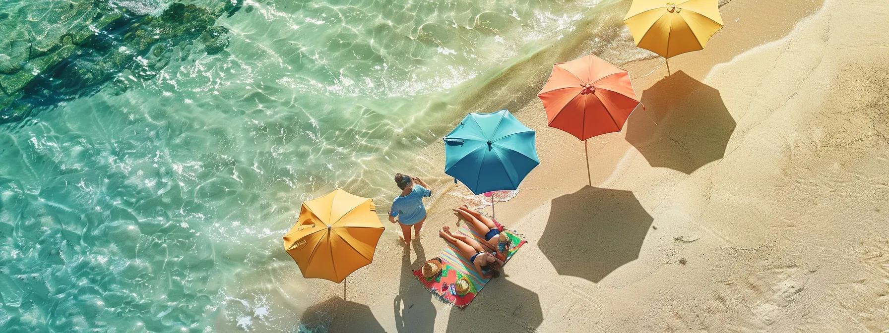 a family picnicking on the beach, surrounded by colorful umbrellas and playing in the clear blue ocean water.